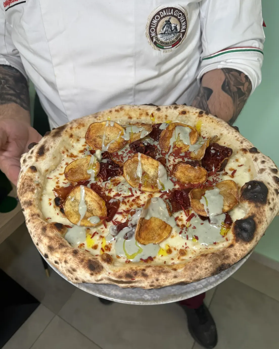 Il pizzaiolo regge una pizza appena sfornata